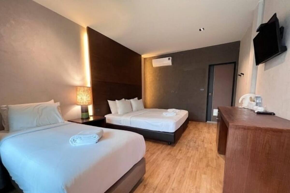 A hotel room with two beds, a desk, a TV, and an air conditioning unit.