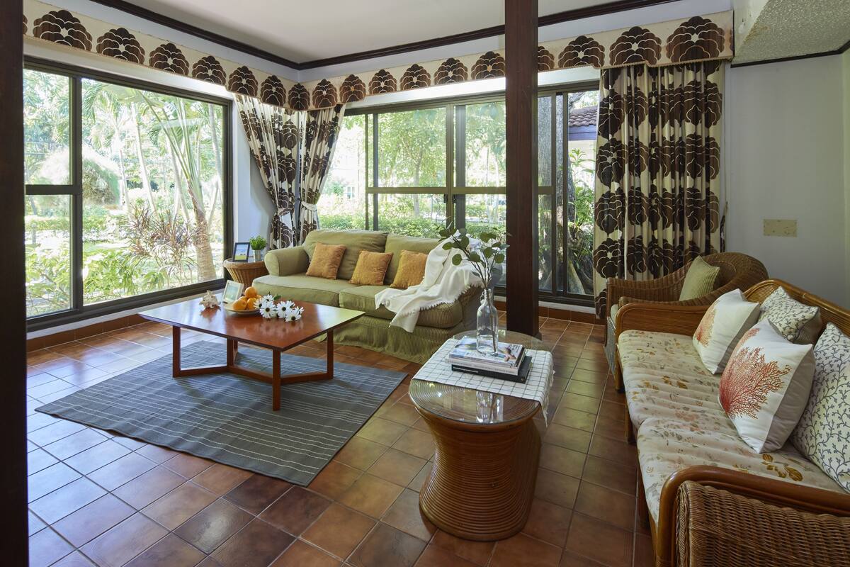 A spacious living room with a green sofa, a wicker sofa, a coffee table, and a large window with curtains.