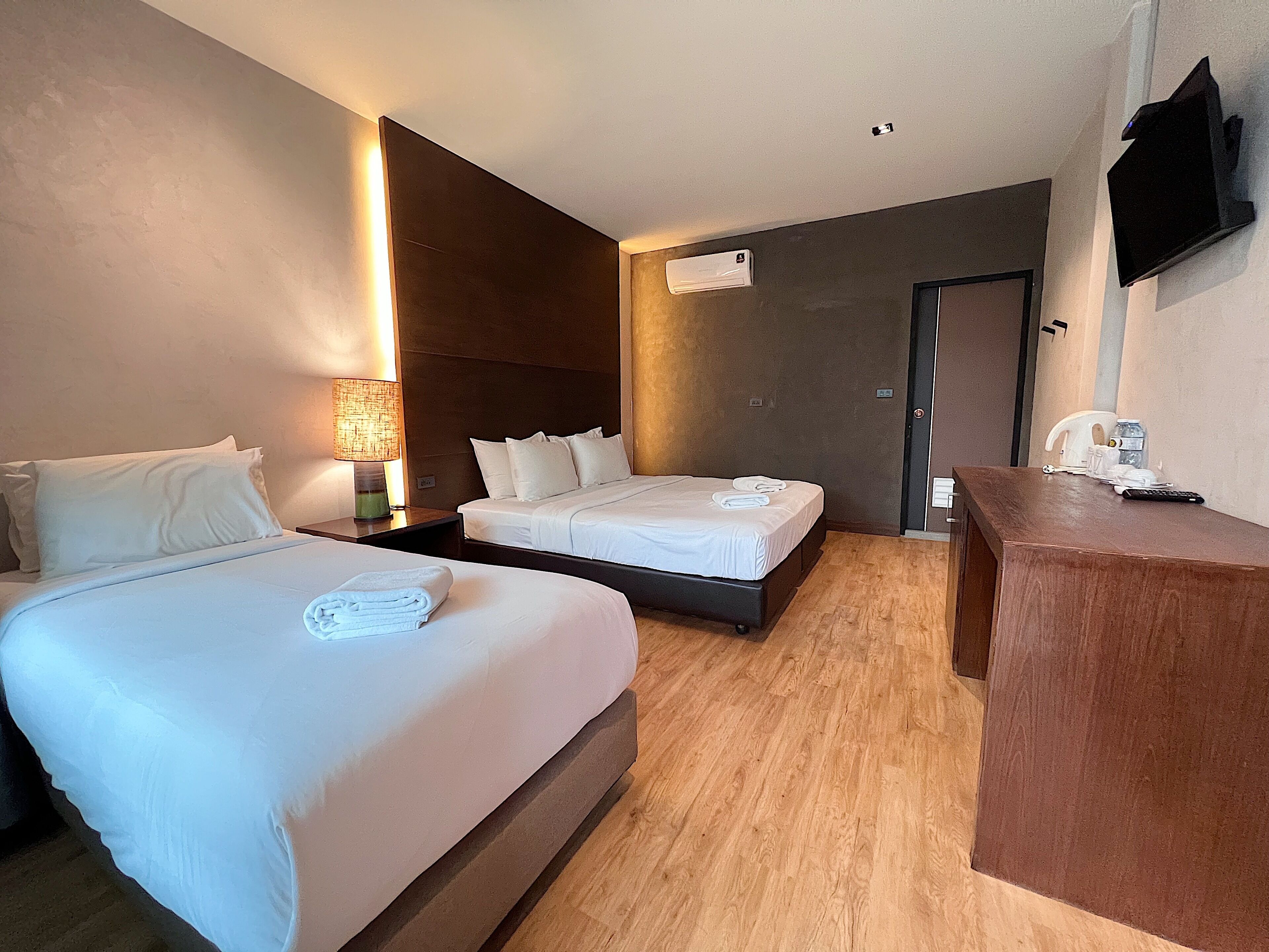 Ein Hotelzimmer mit zwei Betten, einem Holztisch, einem Fernseher und einer Wandklimaanlage.