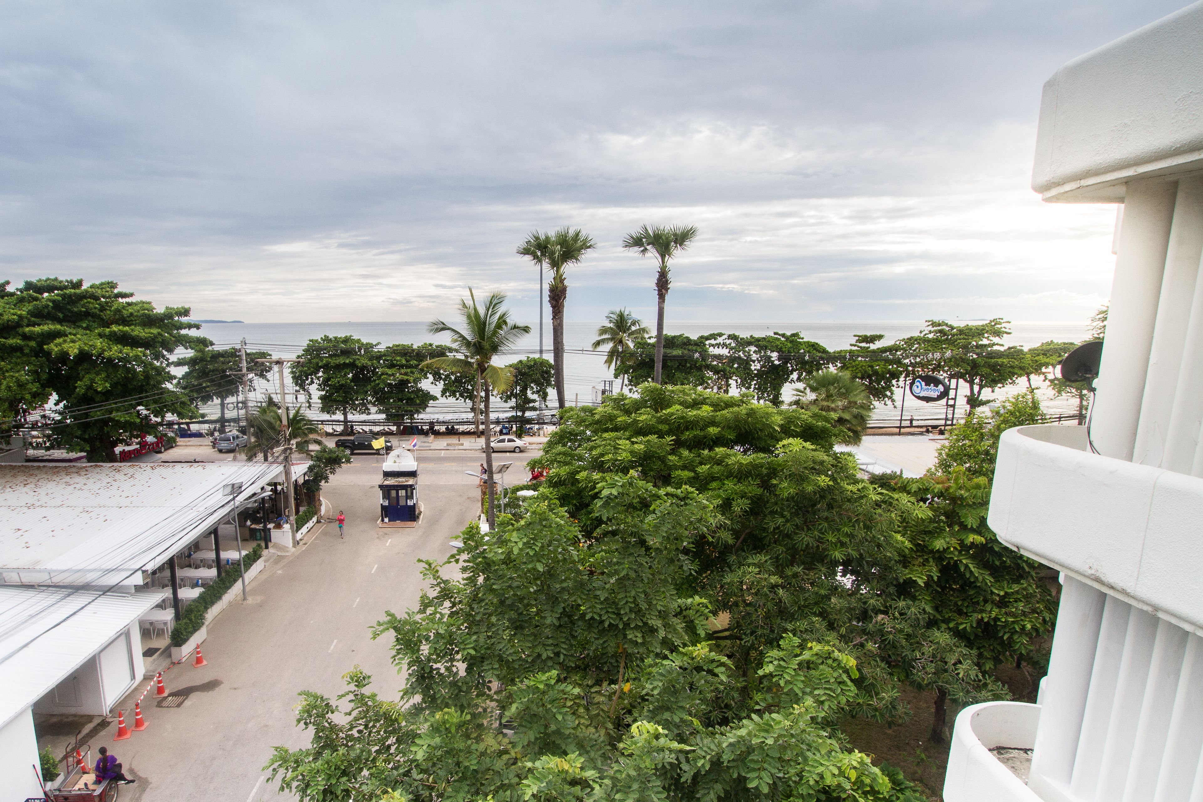 Una calle costera con palmeras, un pequeño quiosco y vista al mar.