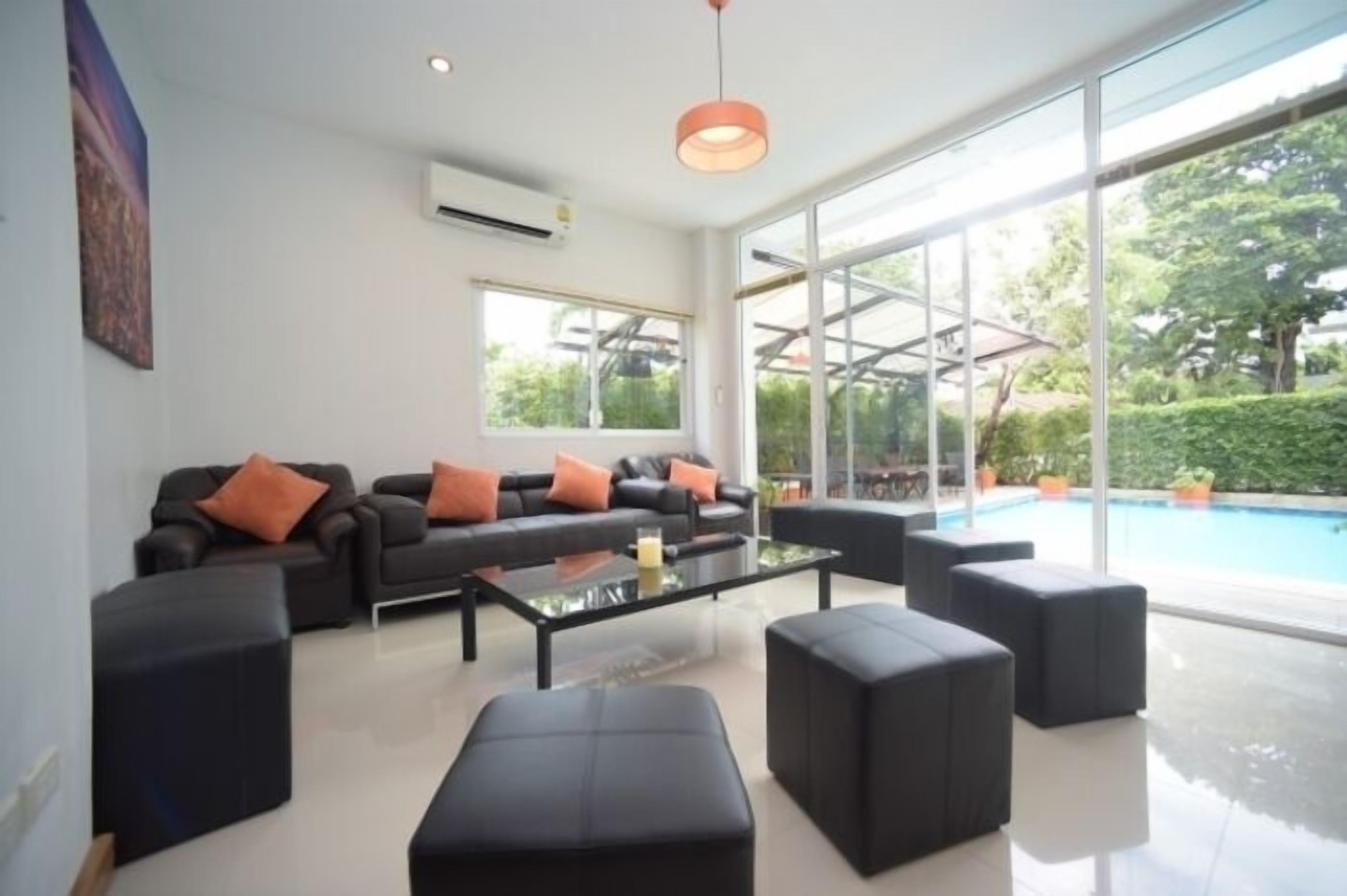 A modern living room with a glass wall, black furniture, and a pool view.