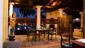 Un espacio exterior para comer con piscina, mobiliario de madera y columnas decorativas.