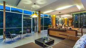 A modern interior with a reception desk, seating area, and large windows offering a view of the outdoors. - Presidential Penhouse - Kamala (Kamala)