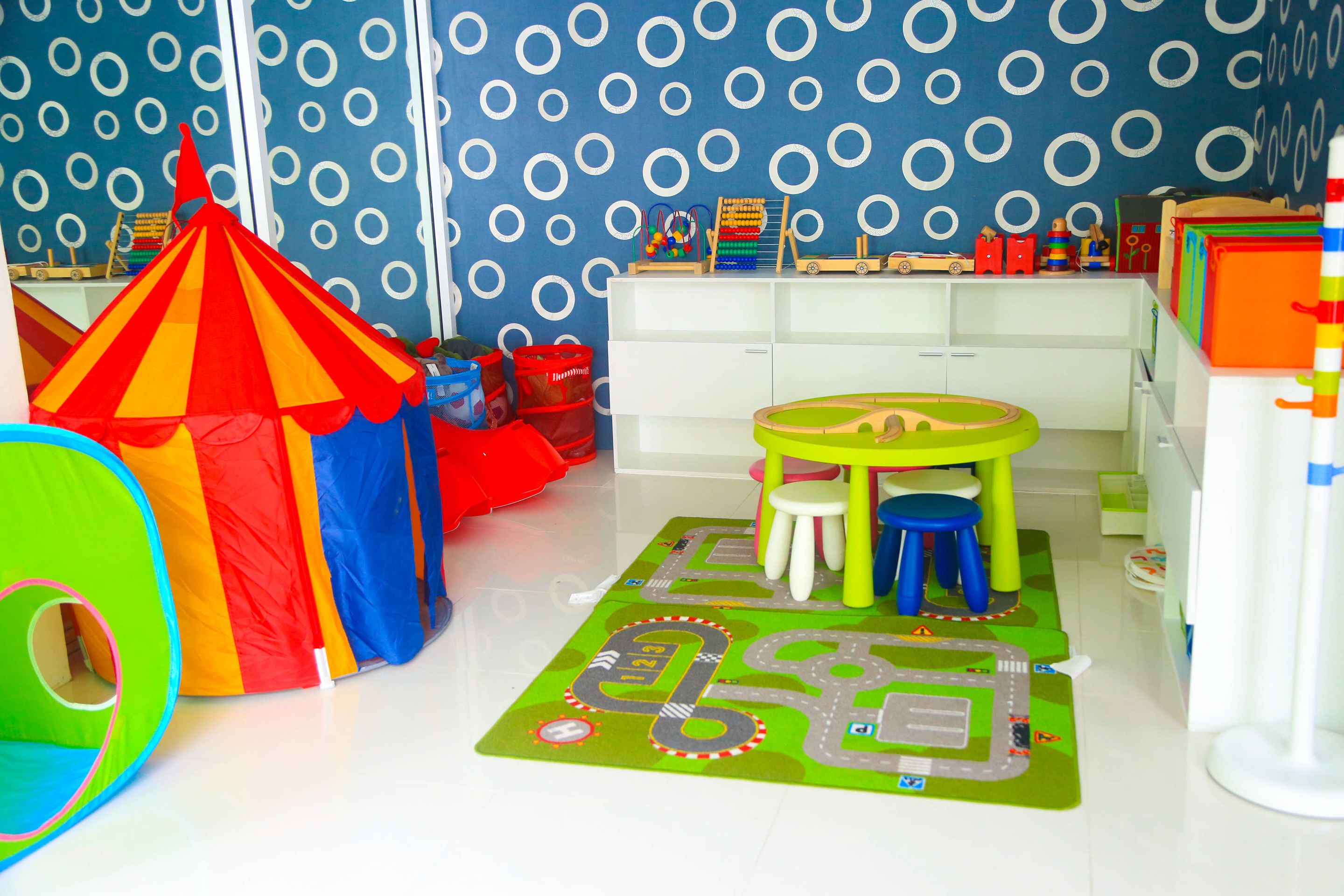 Een speelkamer met een kleurrijke tent, een speelmat en een wit opbergmeubel.