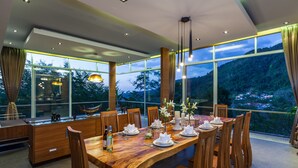A dining area with a wooden table set for six, large windows with a view of a mountainous landscape, and modern pendant lighting. - Presidential Penhouse - Kamala (Kamala)