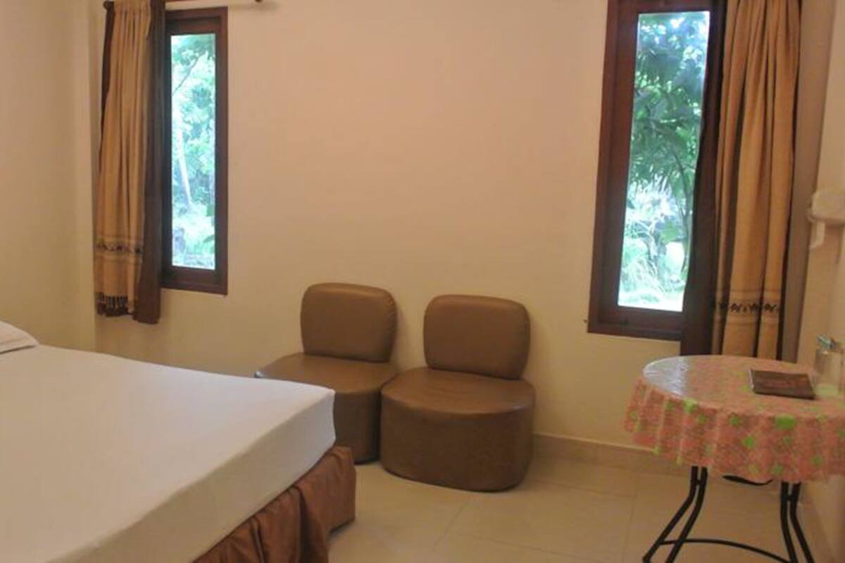 A bedroom with a bed, two chairs, a small table, and windows with curtains.
