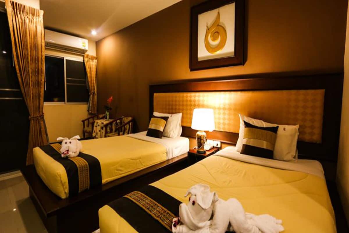 A hotel room with two beds, each with a yellow bedspread and a black and gold accent. There is a framed artwork above the beds, a nightstand with a lamp, and a window with curtains.