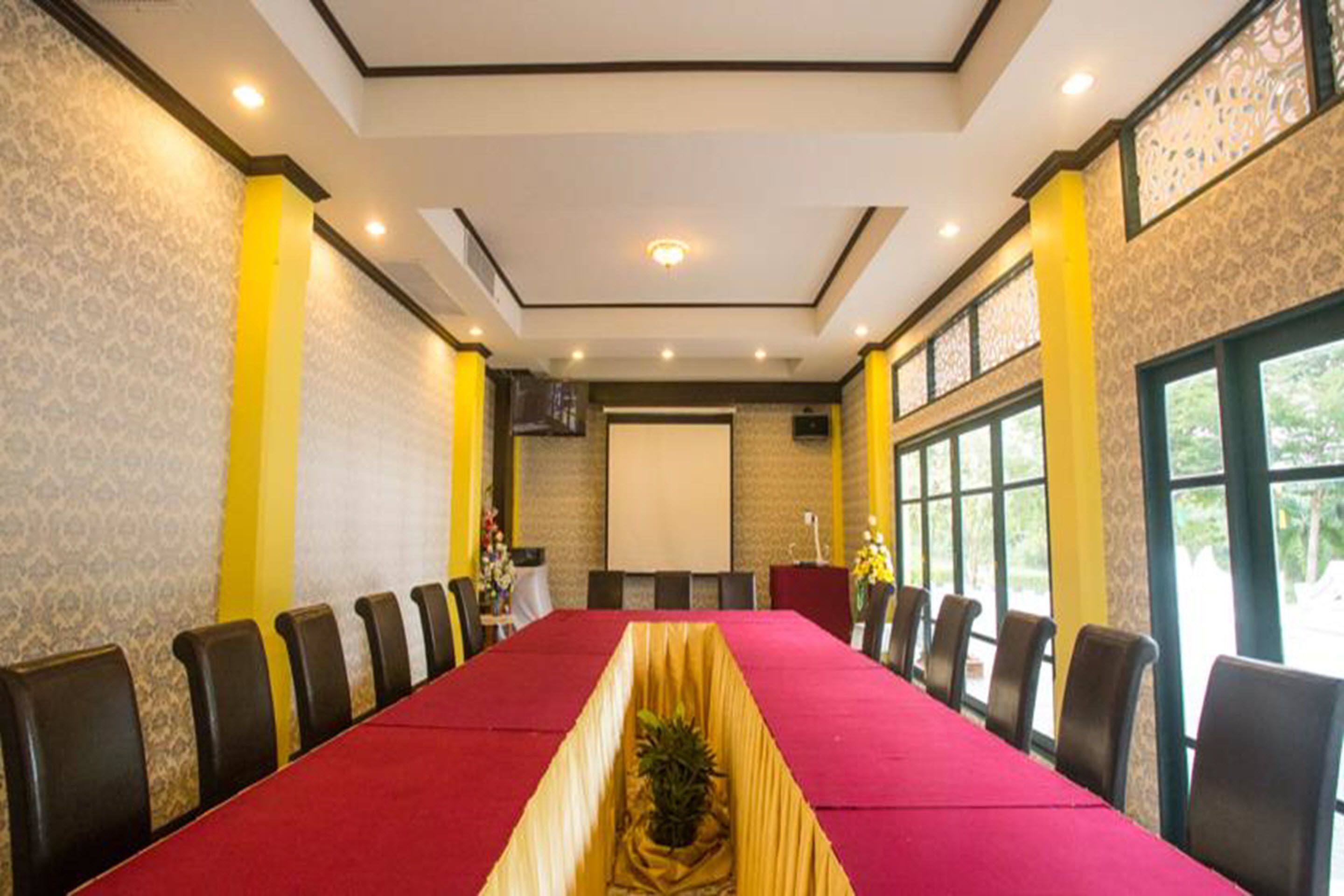 Un salón de conferencias con una mesa larga, sillas, una pantalla de proyector y un ventanal grande.