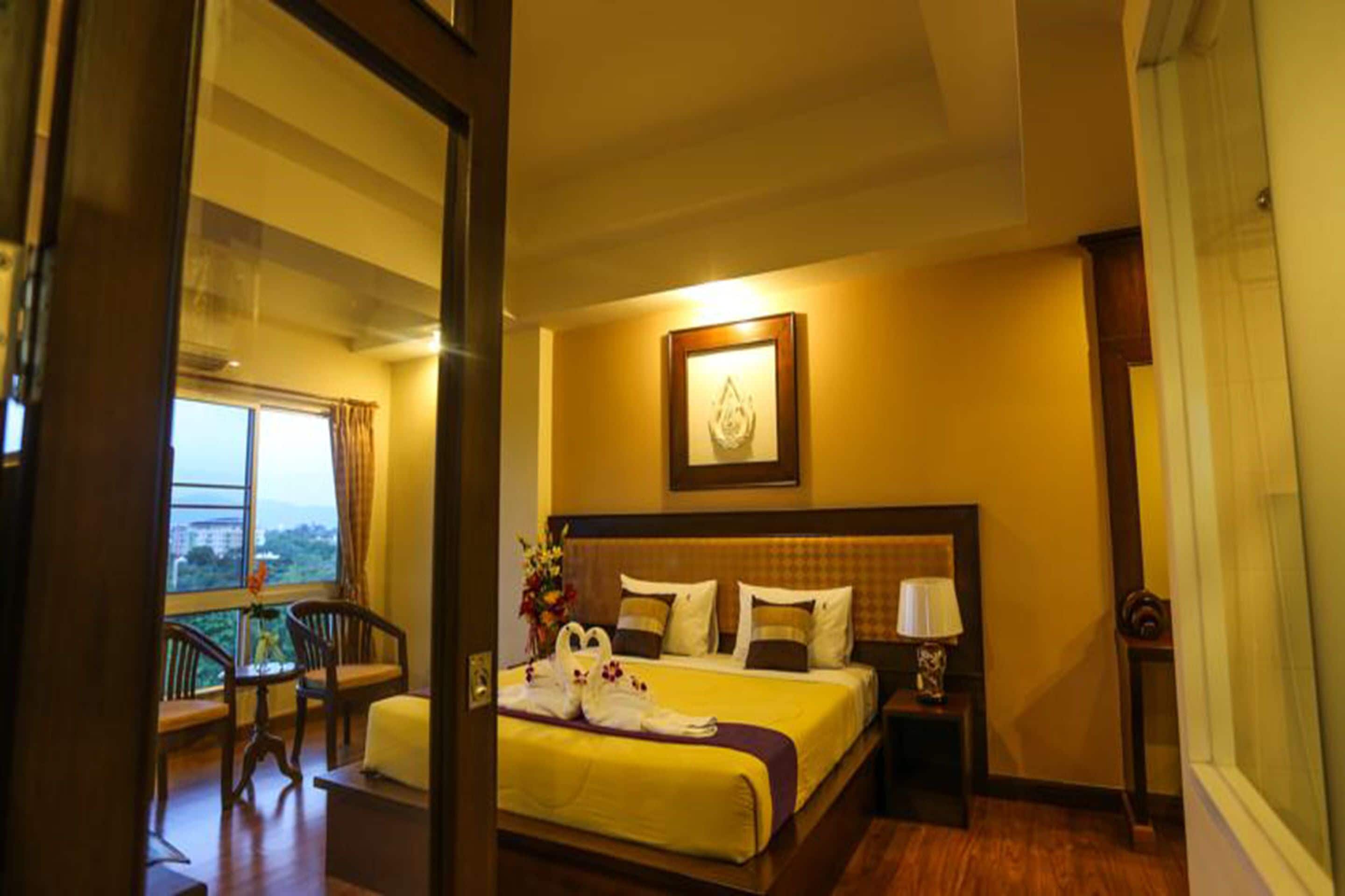 Une chambre d’hôtel avec un lit, une table de chevet, une lampe, un tableau encadré au mur et une vue sur la ville par la fenêtre.
