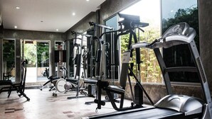 A gym with various exercise equipment, including treadmills and weight machines, with large windows providing natural light. - Madina Hotel (Rayong)