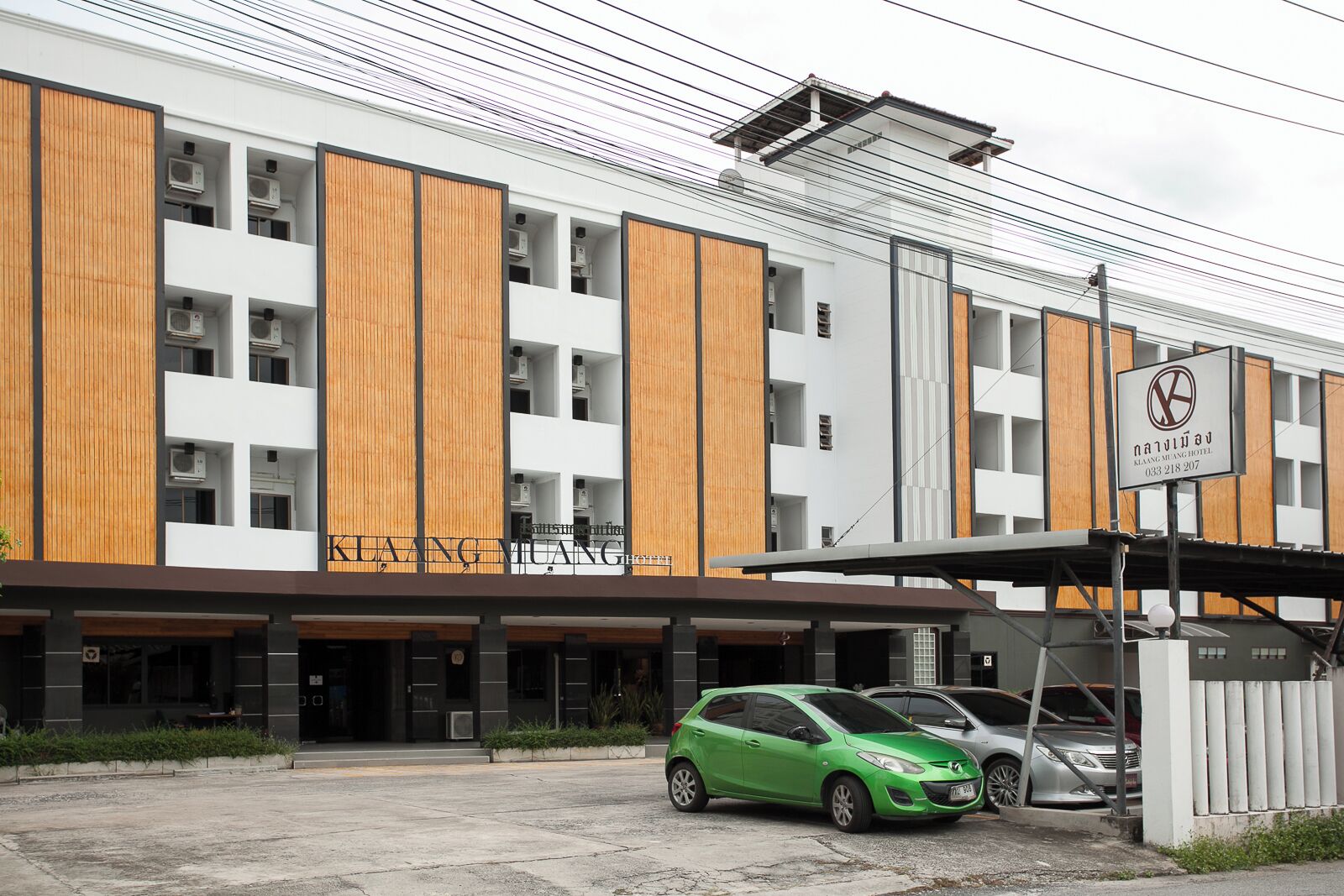 Un hotel moderno con fachada blanca y detalles de madera, que destaca por su entrada principal y un coche verde estacionado al frente.
