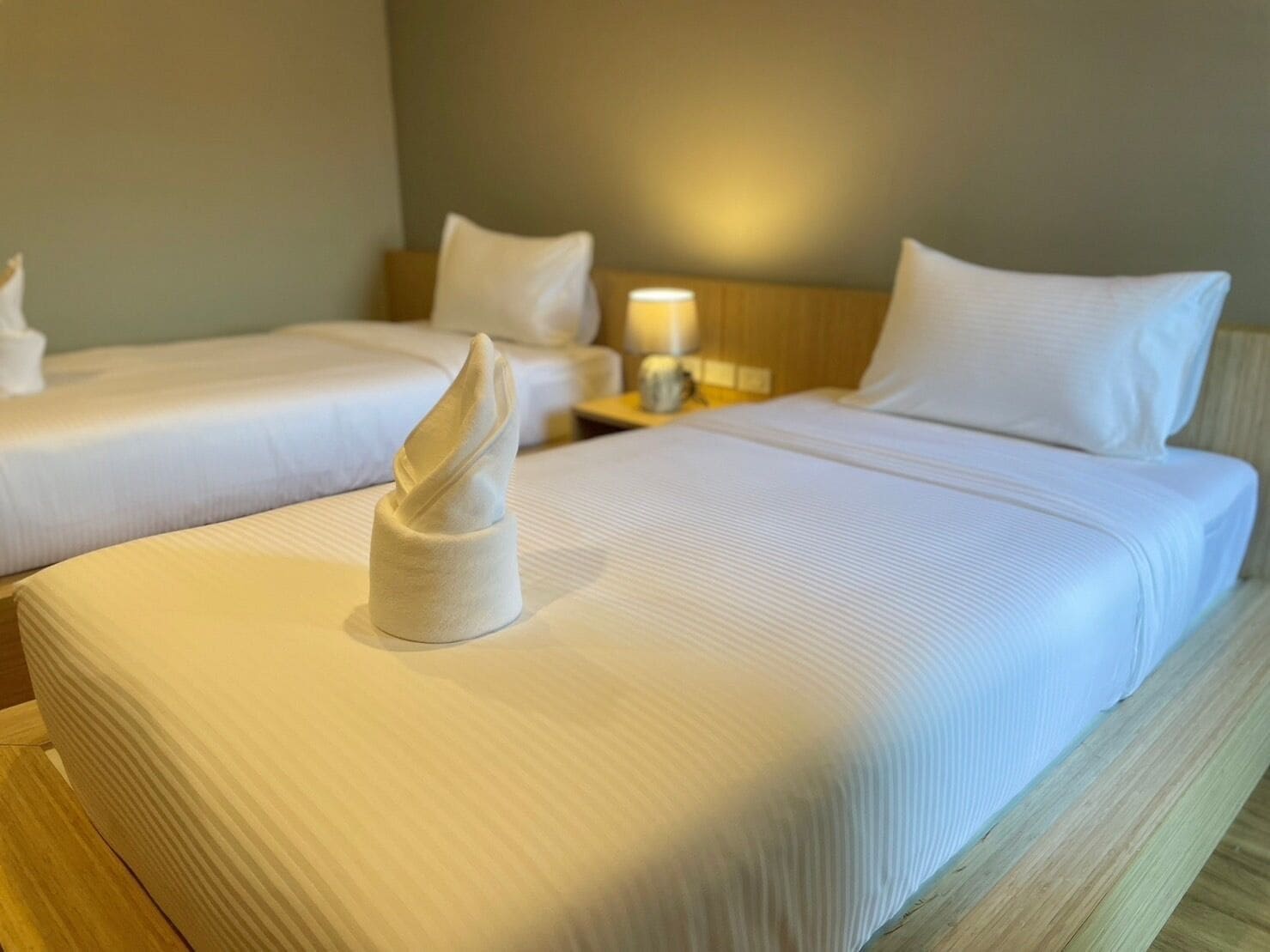 A hotel room with two beds, each with white linens and pillows, and a neatly folded towel on the bed.