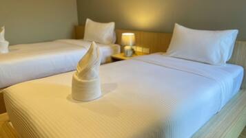 A hotel room with two beds, each with white linens and pillows, and a neatly folded towel on the bed.