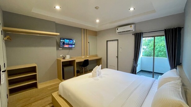 Una habitación de hotel moderna con una cama grande, un escritorio con una computadora, un televisor y un balcón con cortinas.
