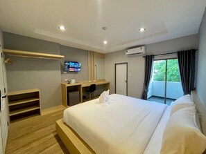 A modern hotel room with a large bed, a desk with a computer, a TV, and a balcony with curtains.