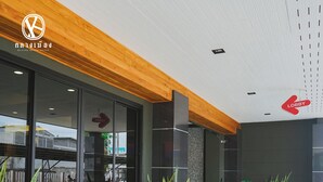 Un moderno vestíbulo de hotel con techo de madera, plantas en macetas y un cartel que indica el área de recepción.