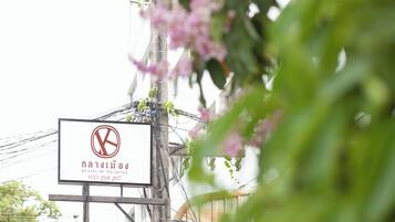 A hotel sign with a logo and name in Thai script, surrounded by greenery and power lines.