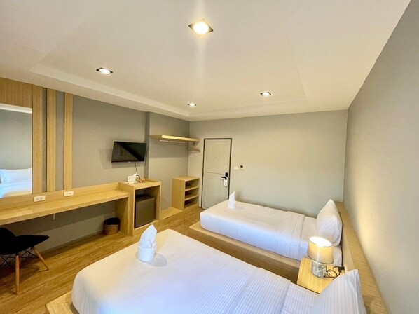 A hotel room with two beds, a desk, a TV, and a shower area.