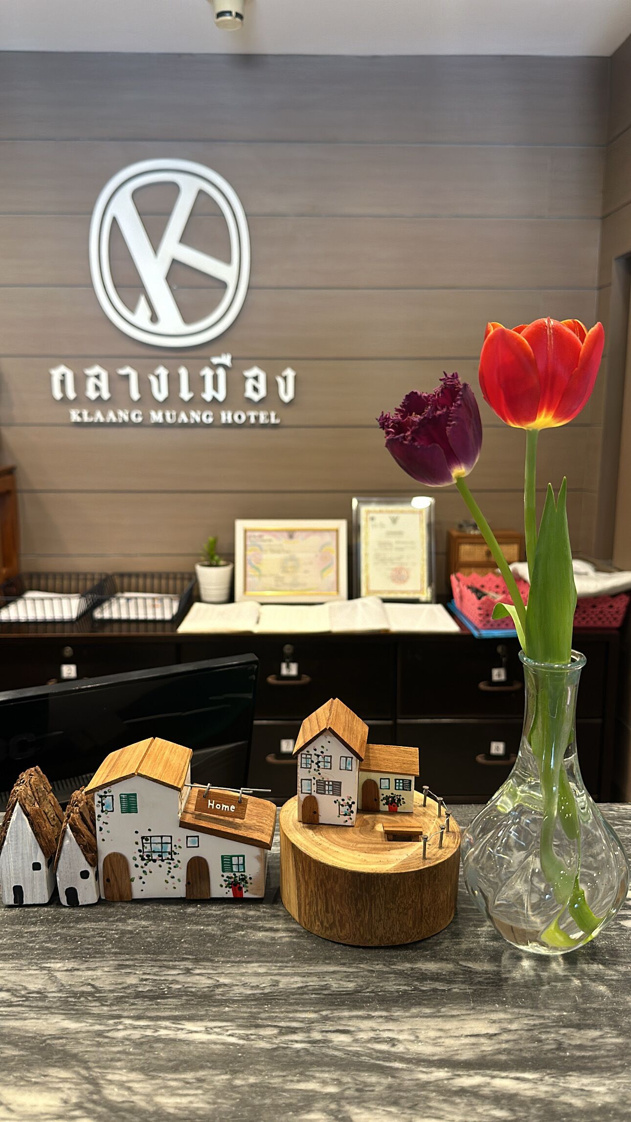 Un mostrador de recepción con un logotipo, un jarrón con tulipanes y casitas en miniatura.