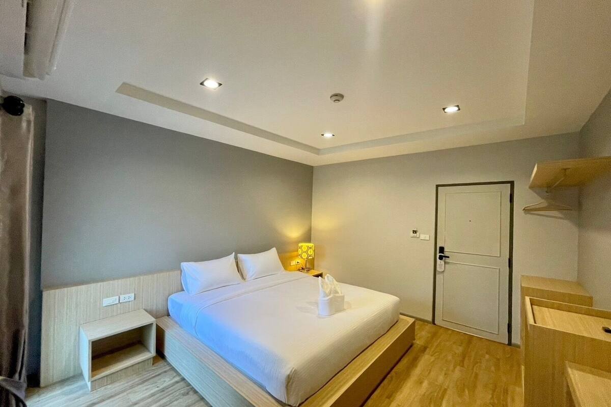 Een hotelkamer met een bed, nachtkastje, lamp en een deur.