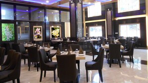 Un restaurante espacioso con numerosas mesas y sillas, amplias ventanas que permiten la entrada de luz natural y decoración mural decorativa.