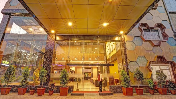Entrada de hotel con diseño moderno, que presenta fachada de vidrio, pared con patrón geométrico y plantas en macetas.