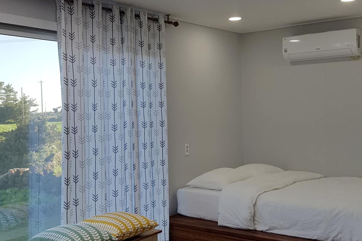 Une chambre à coucher comprenant un lit, un banc, une fenêtre avec des rideaux et un appareil de climatisation.