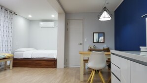 Une chambre moderne avec un lit, une table de chevet et un bureau avec une chaise. On y trouve une fenêtre avec des rideaux, un luminaire au plafond et un climatiseur fixé au mur.