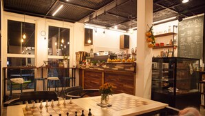 Un café chaleureux avec un échiquier posé sur une table, un menu écrit à la craie et une vue dégagée grâce à de grandes fenêtres.