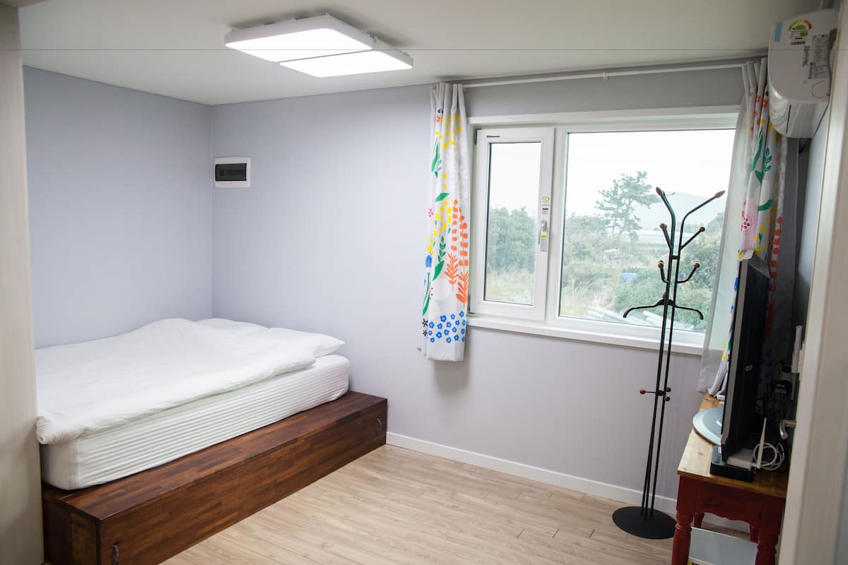 Une chambre à coucher avec un lit, une fenêtre, un téléviseur et un porte-manteau.