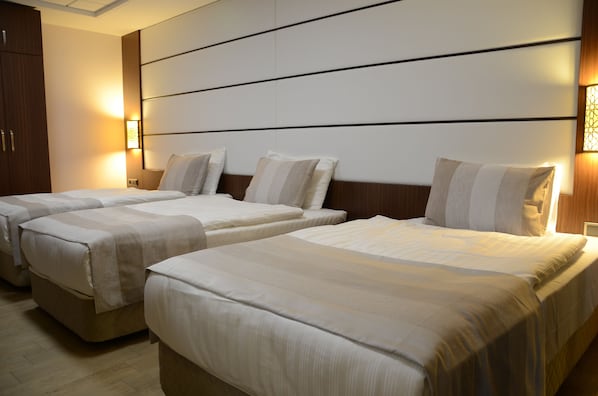 Habitación de hotel con tres camas dispuestas en fila, cada una con cabecero y lámparas de noche.