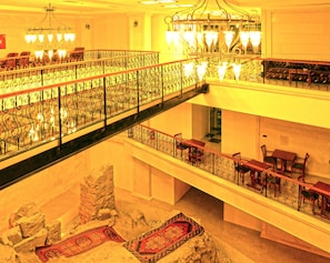 Un vestíbulo de hotel de varios niveles con barandillas decorativas, candelabros y una escalera central.