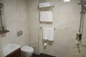 Een badkamer met een douchecabine van glas, toilet, wastafel en twee handdoekrekken met handdoeken.