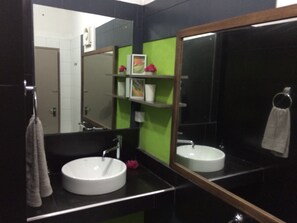 A bathroom with a round white sink, a mirror, and a green accent wall.