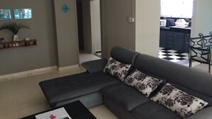 A living room with a grey sectional sofa, a small coffee table, and a decorative shelf with plants. - Seaview Holiday Apartments (Grand-Baie)