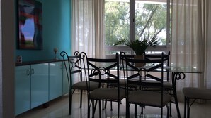 A dining area with a glass table and chairs, a potted plant, and a view of trees through the window. - Seaview Holiday Apartments (Grand-Baie)