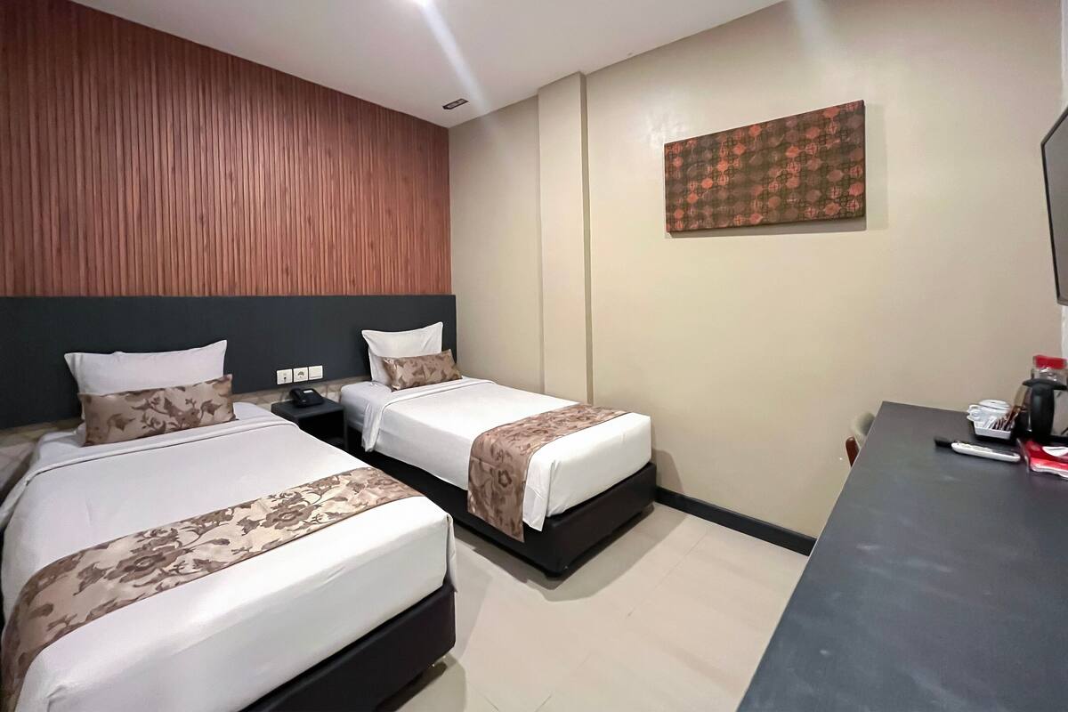 A hotel room with two single beds, a wooden headboard, a flat-screen TV, and a desk with a coffee maker.
