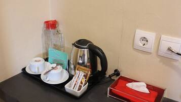 A hotel room's breakfast setup with a coffee maker, a bottle of water, a tray with a cup and saucer, a box of tea bags, and a tissue box.