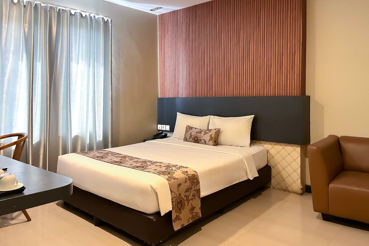 A hotel room with a bed, a desk, a chair, and a wall with vertical wooden slats.