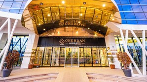 Exterior del Hotel Gherdan Gold, con fachada de vidrio moderna y un llamativo marquesina dorada.