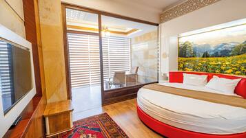 Une chambre à coucher moderne avec un lit aux lignes courbes, une grande fenêtre avec des stores, un téléviseur et un tapis décoratif.