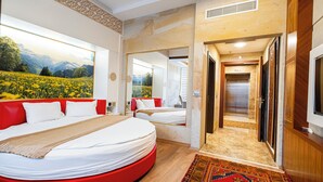 Una habitación de hotel moderna con una cama grande, una pared de acento roja, un ventanal con vistas a la montaña y un pasillo que conduce a un ascensor.