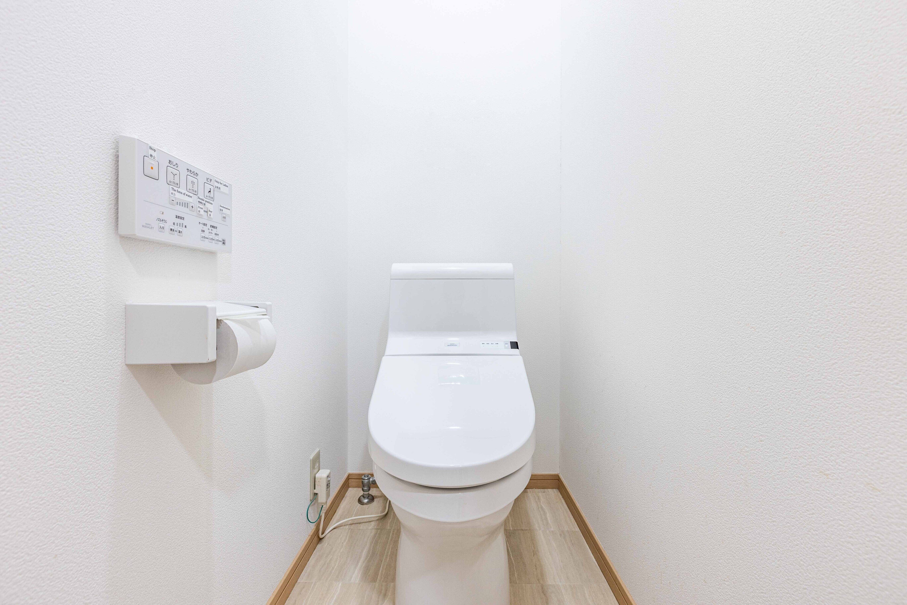 A small, clean bathroom with a toilet, a wall-mounted toilet paper holder, and a visible electrical outlet.