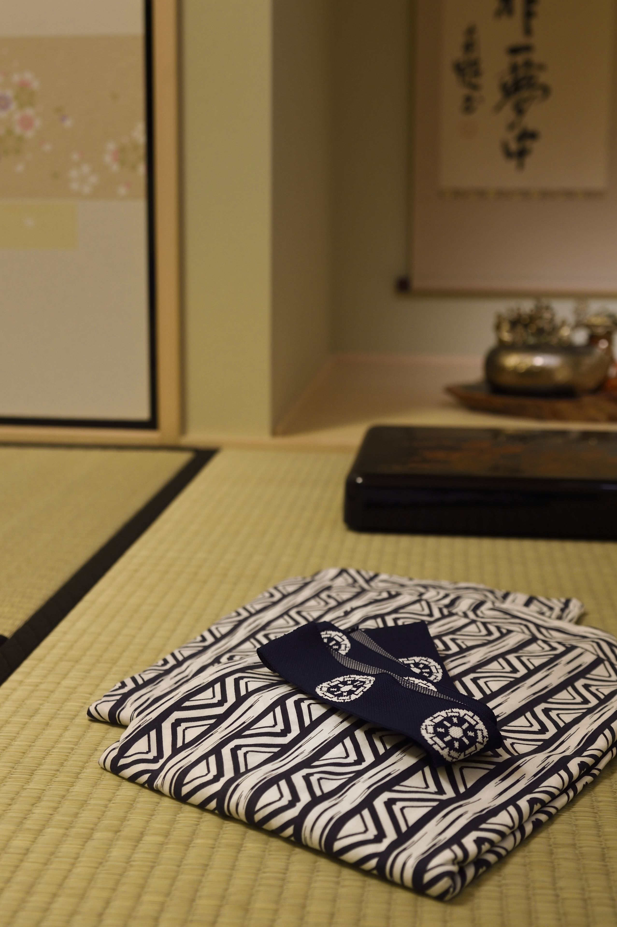 A neatly folded traditional Japanese garment with a geometric pattern, placed on a tatami mat.