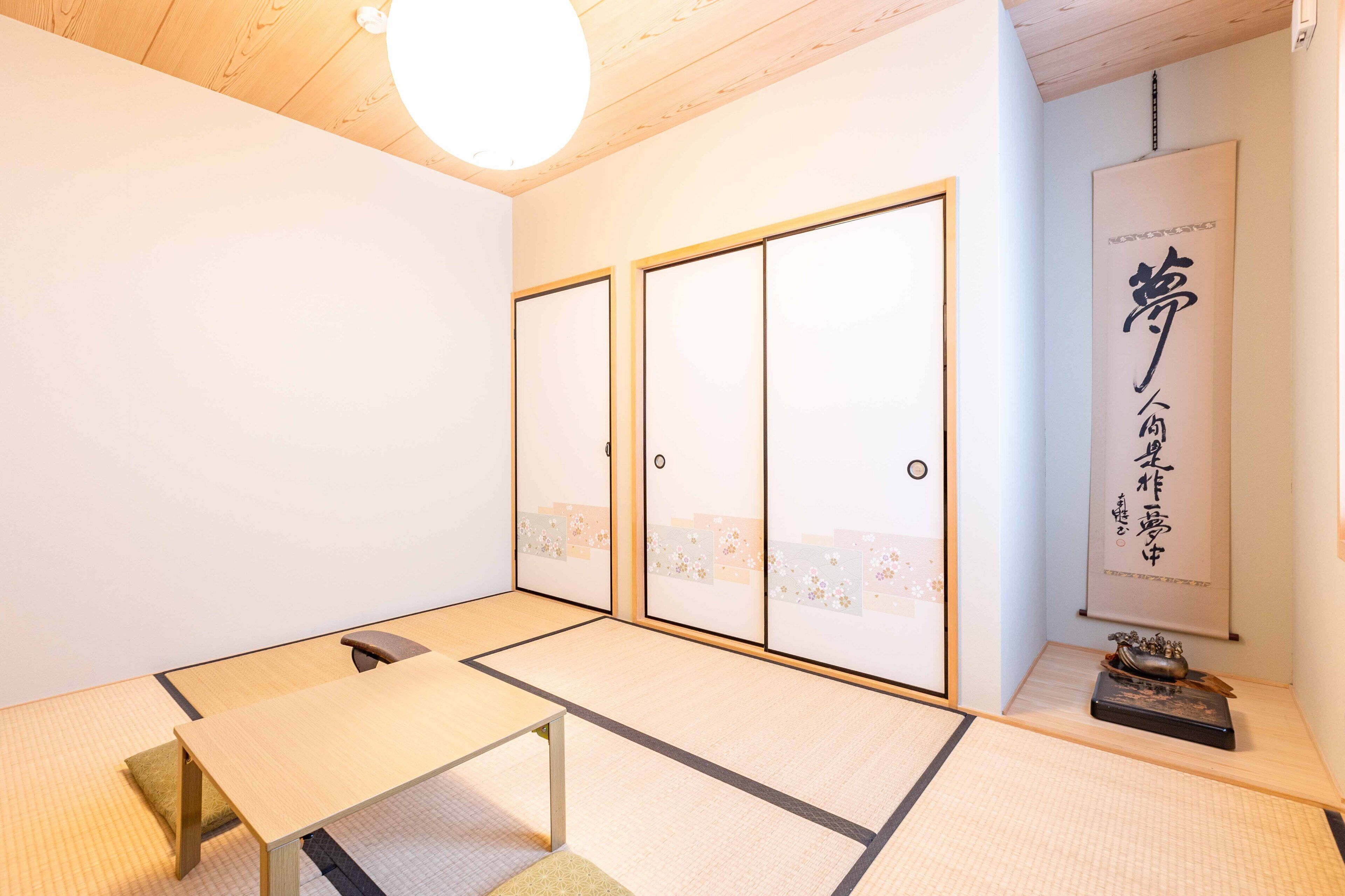 A traditional Japanese room with tatami flooring, a low table, sliding doors, and a hanging scroll.