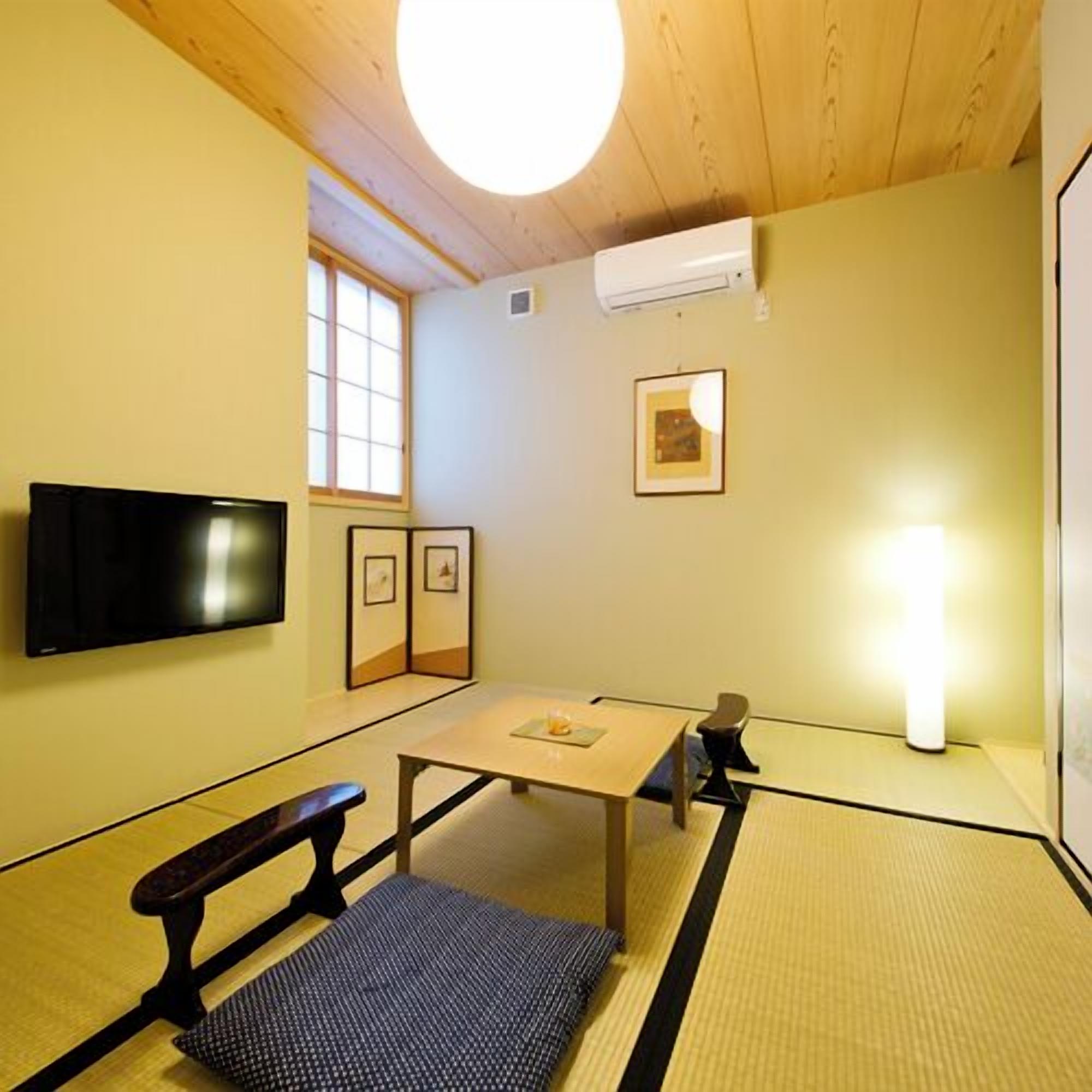 A tatami mat room with a television, a table, a bench, and a picture frame on the wall.