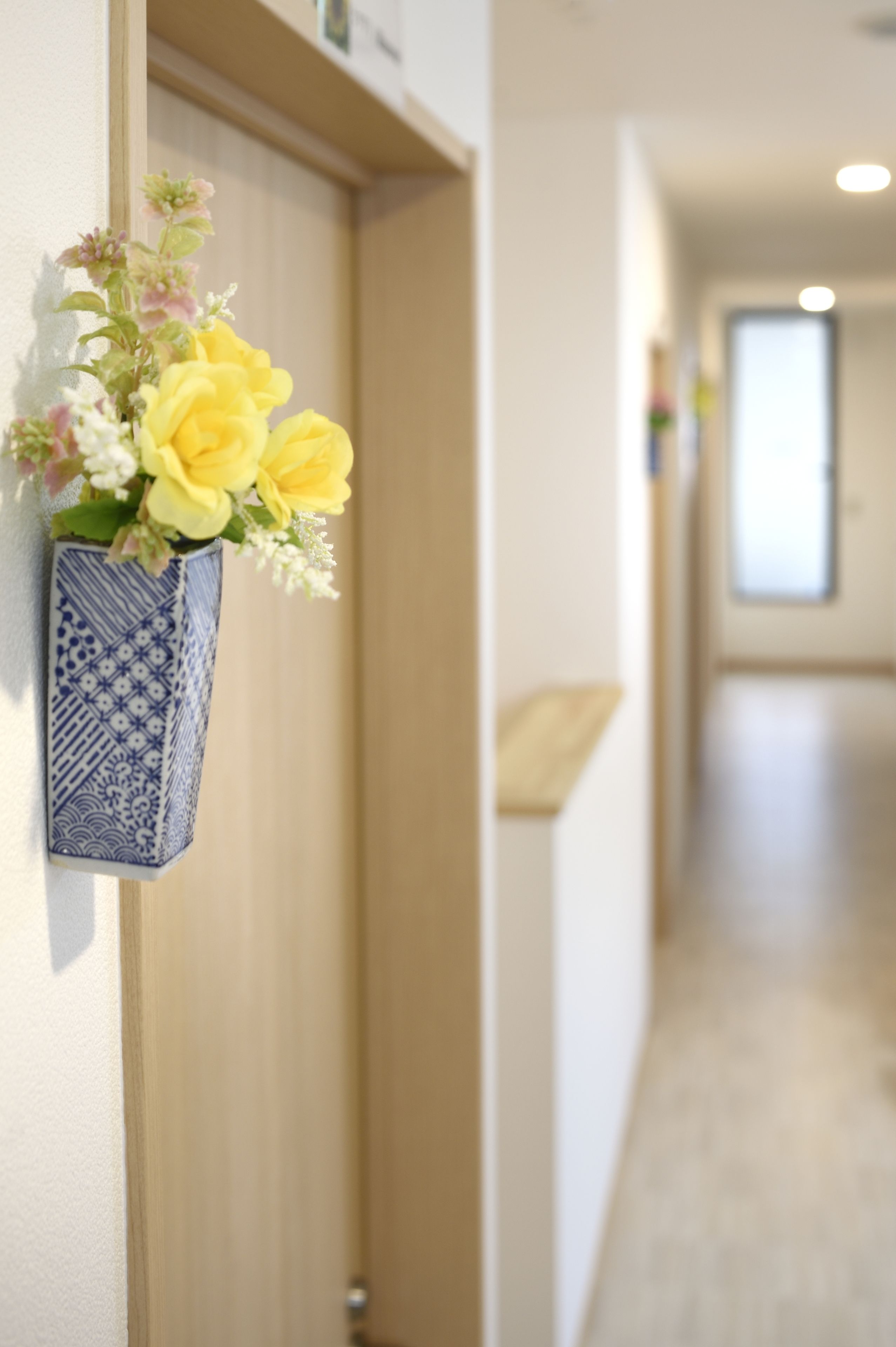 A hallway with a blue vase containing yellow flowers on the wall.