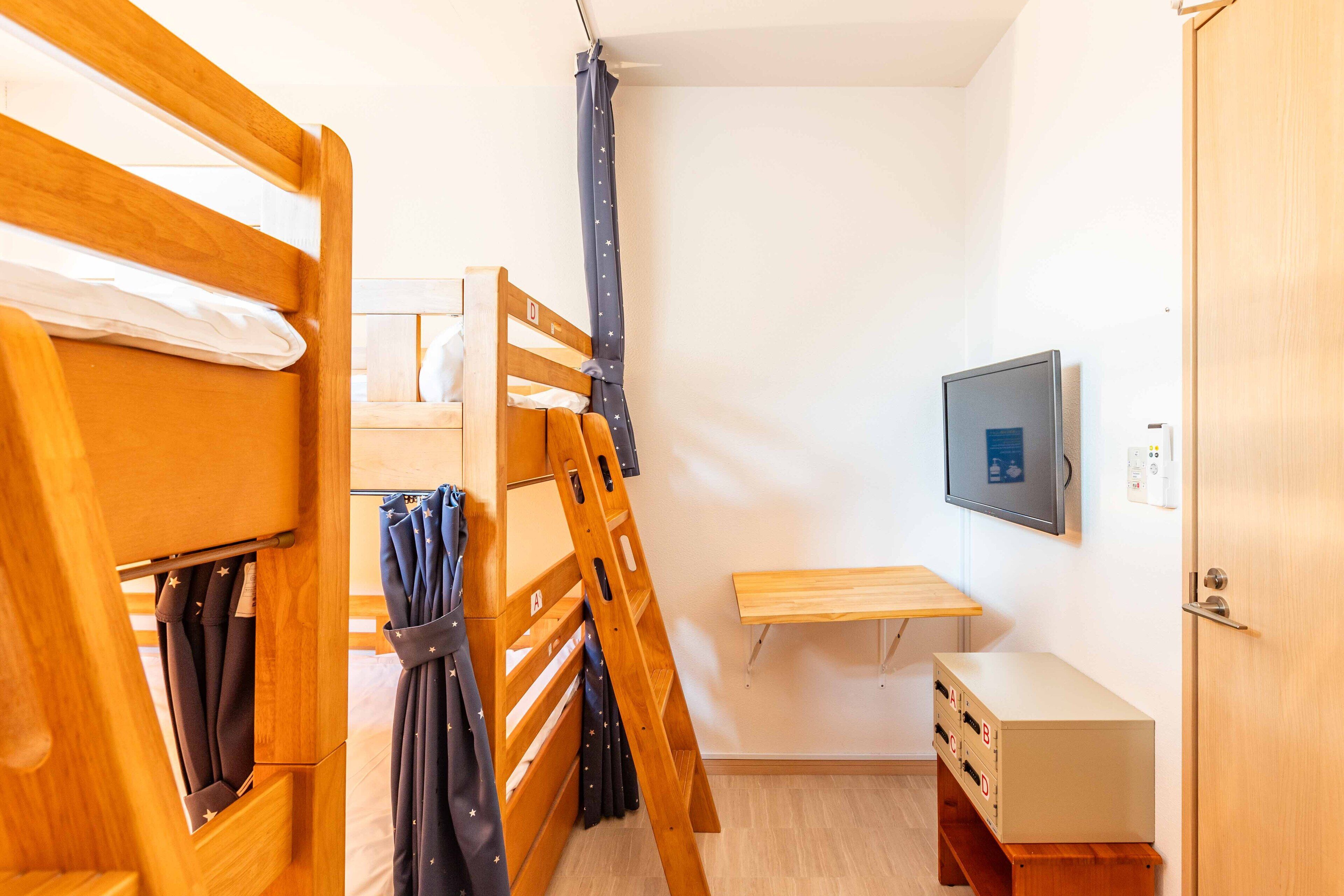 A dormitory room with bunk beds, a desk, a chair, and a television.