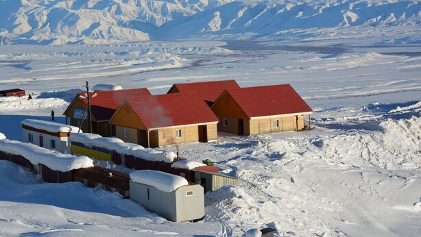 Een groep houten gebouwen met rode daken in een besneeuwd landschap.