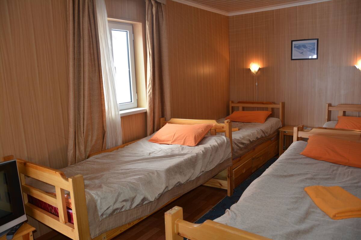 Una habitación con dos camas de madera, una ventana con cortinas, un escritorio con computadora y un cuadro enmarcado en la pared.